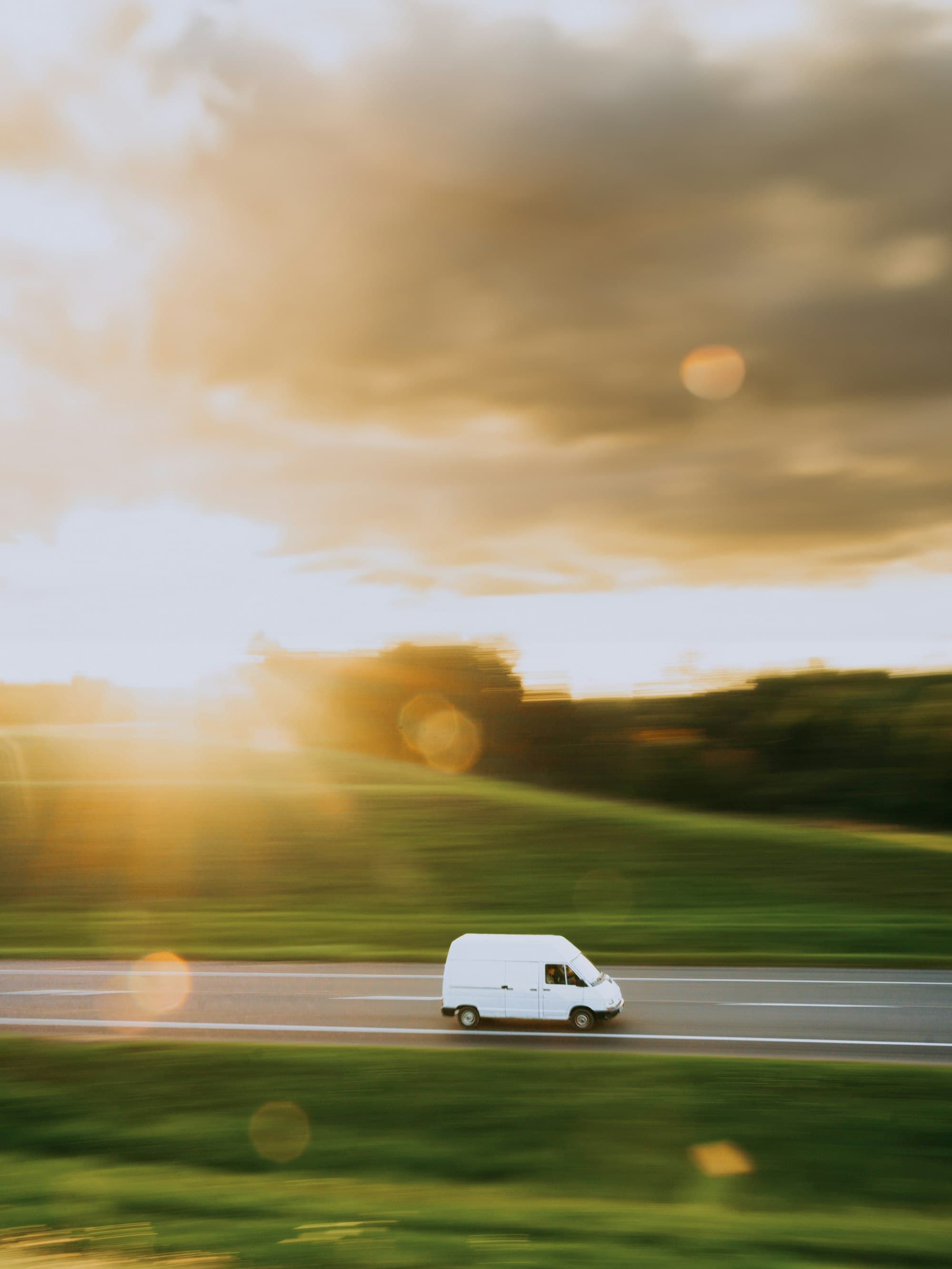 A white van driving along an open road through green hills at sunset